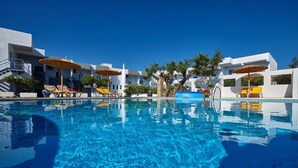 Piscina azul cristalina con tumbonas y sombrillas, rodeada de edificios blancos con balcones.