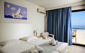 Habitación de hotel con dos camas, un cuadro de un velero, vista al mar a través de ventanas amplias y una silla junto a la ventana.