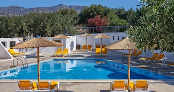 Una piscina con sillas de descanso amarillas y sombrillas de paja, rodeada de follaje y una montaña al fondo.