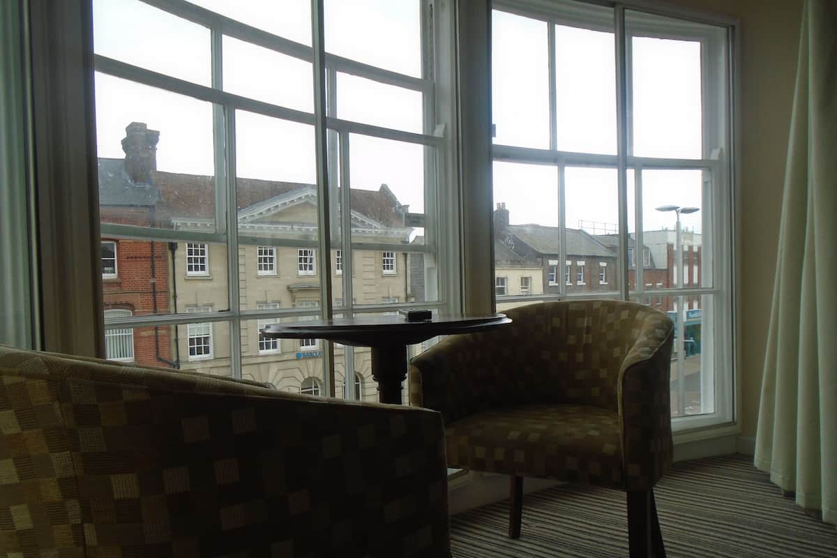 A room with a large window, a patterned sofa, a chair, and a small table.