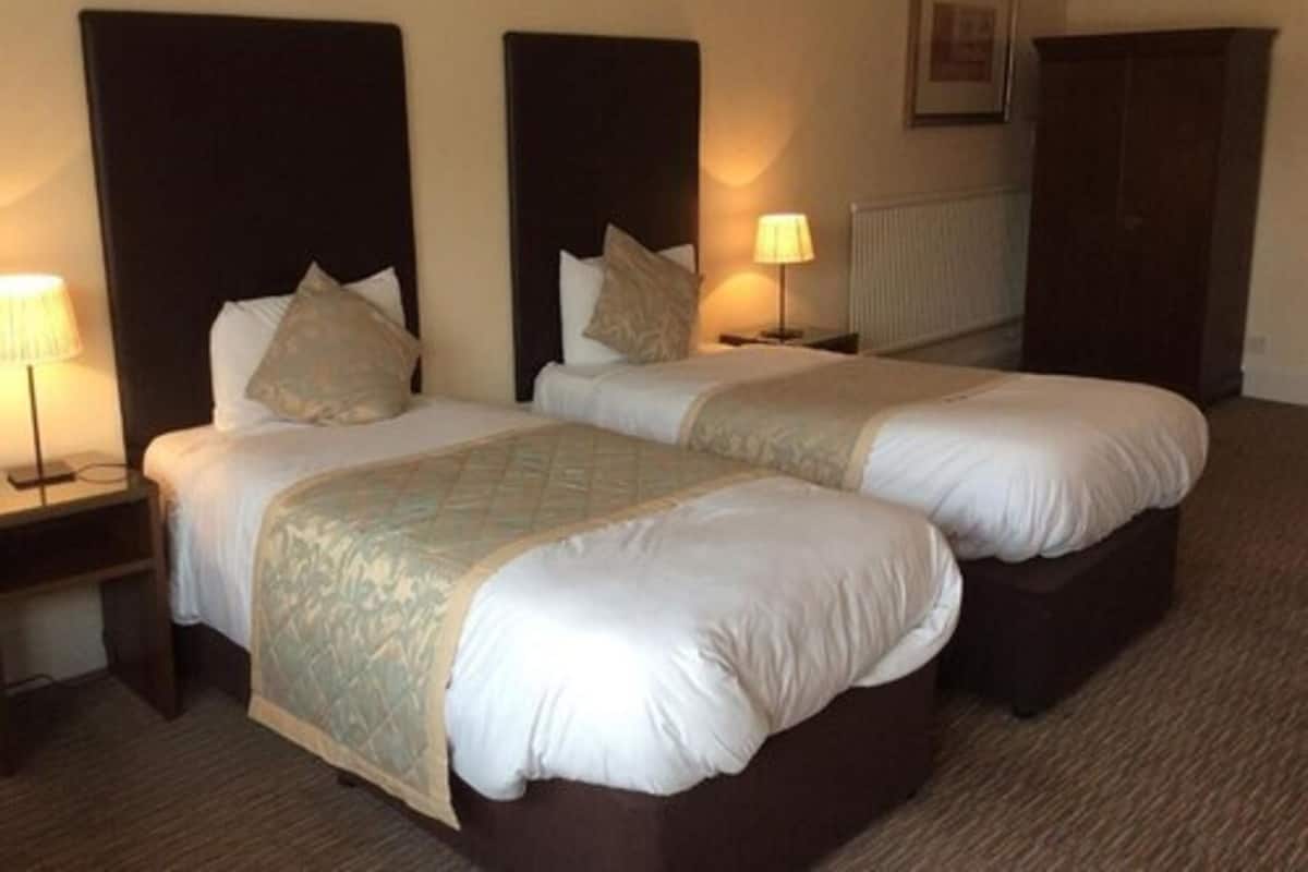 A hotel room with two beds, nightstands with lamps, a radiator, and a dark wooden wardrobe.