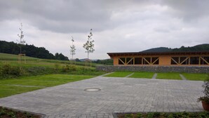 Un bâtiment à la façade en pierre et aux grandes fenêtres, entouré d’une cour pavée avec un petit espace aménagé en jardin.