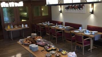 Un comedor con mesas y bancos de madera, una mesa de buffet con alimentos, y un cuadro de un caballo colgado en la pared.