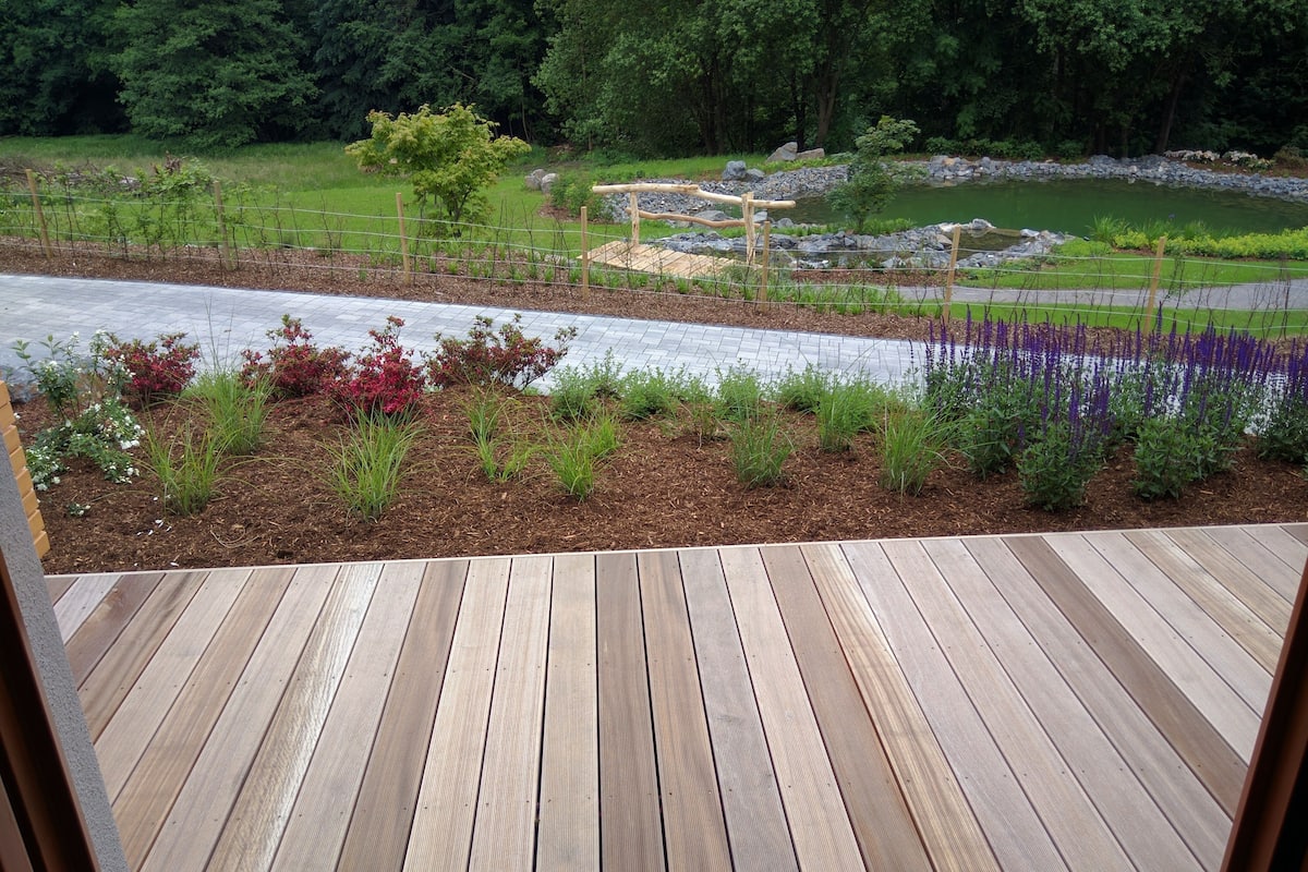 A wooden deck with a view of a landscaped garden area featuring various plants and a small pond.