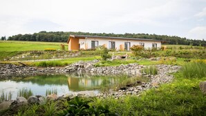 Un bâtiment d’un seul étage, doté d’un toit plat, entouré d’un paysage naturel comprenant un étang et de la végétation.