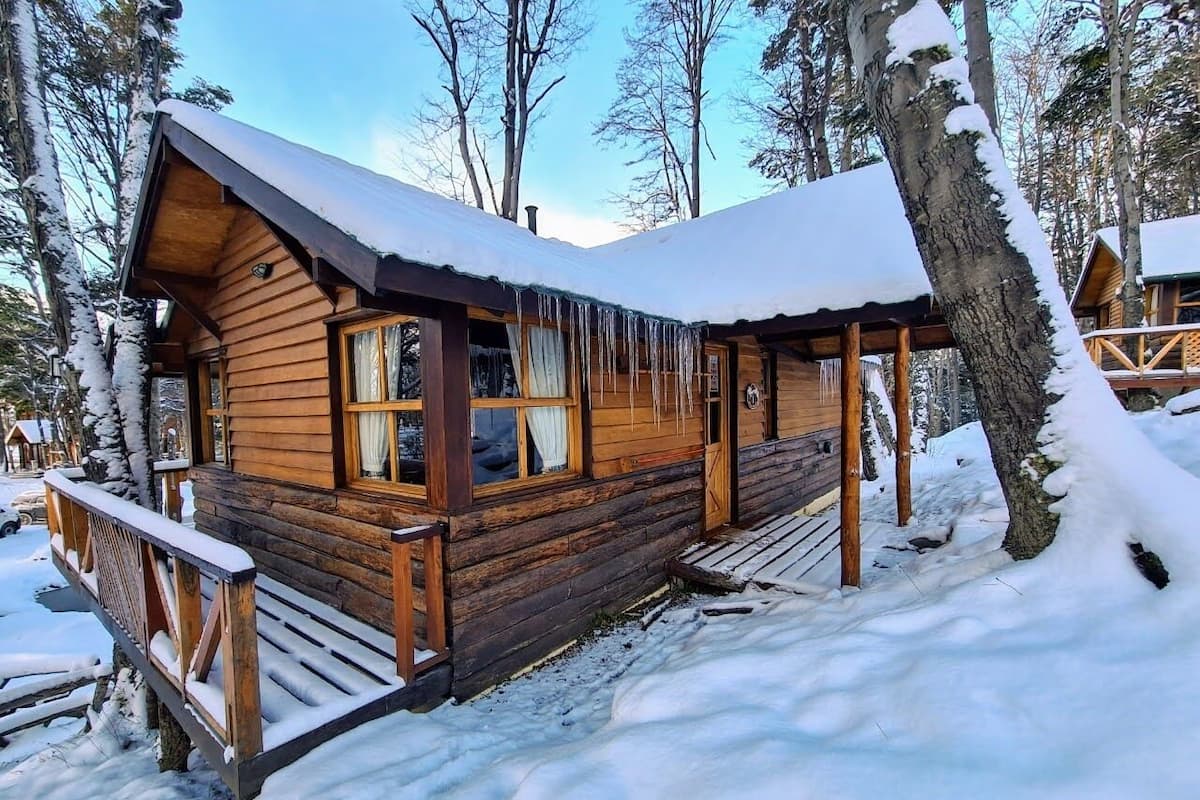 A wooden cabin with a covered porch, surrounded by snow-covered trees.