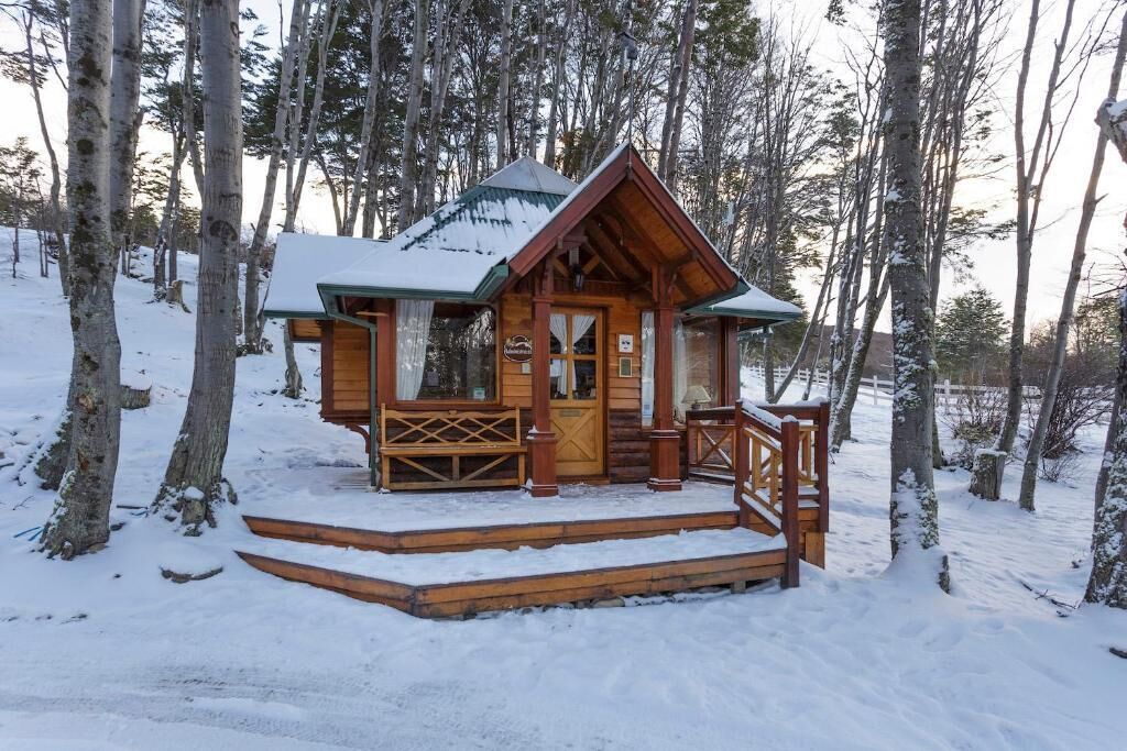 Lumihunnun peittämä puinen mökki, jonka ympärillä on puita.