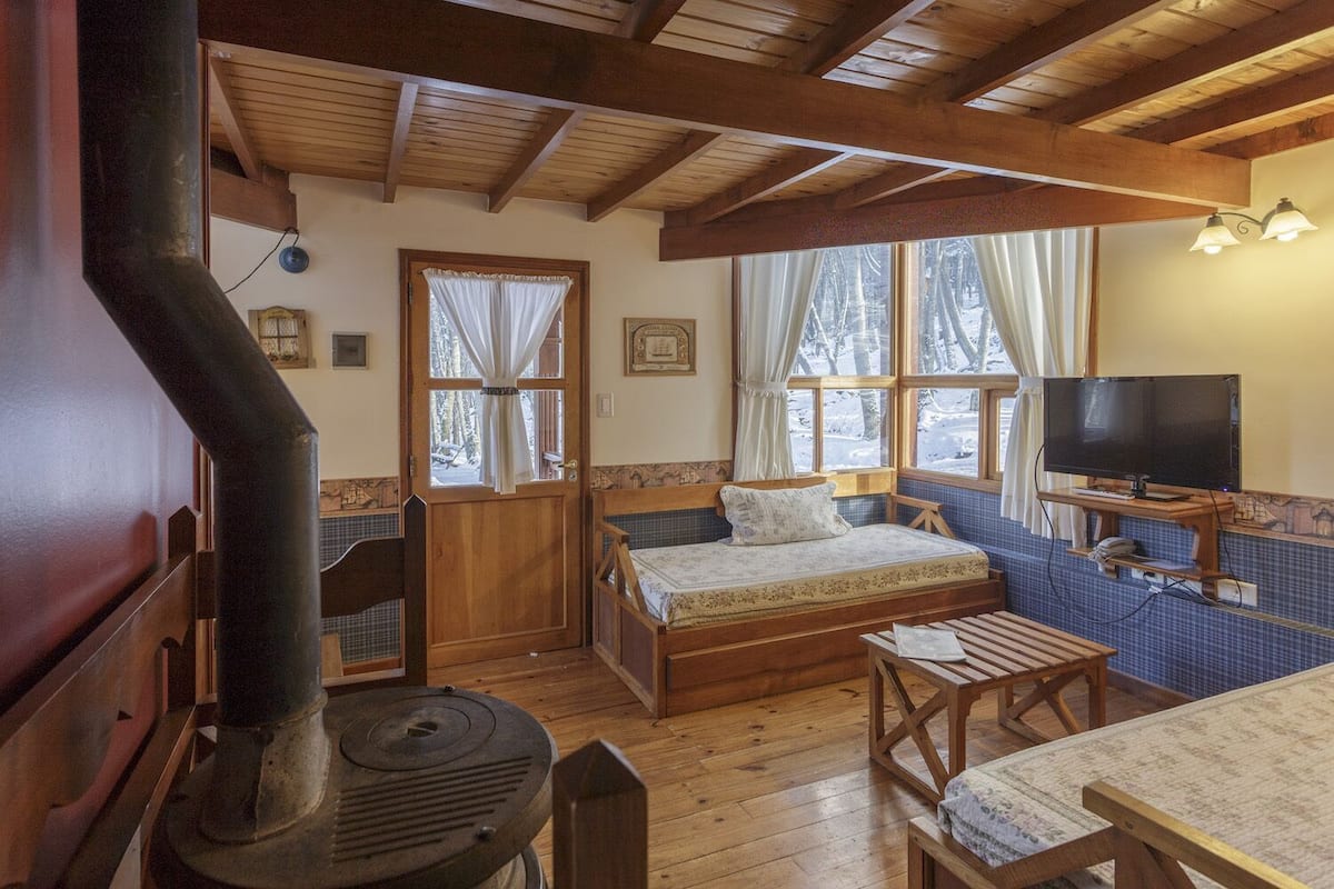 A cozy cabin room with a bed, a television, a fireplace, and a window with curtains.