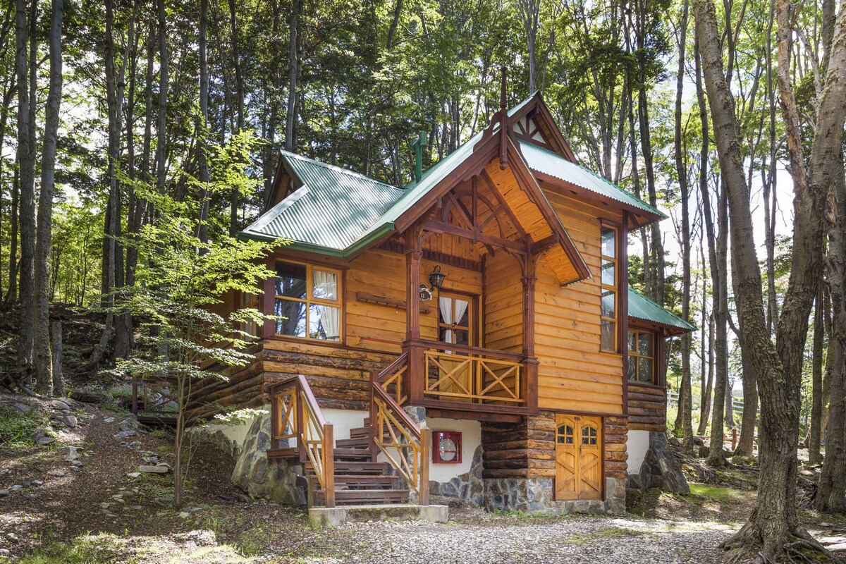 A wooden cabin with a green roof, surrounded by trees.