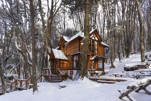 A wooden cabin with a snow-covered roof, surrounded by trees in a forest. - Aldea Nevada (Ushuaia)