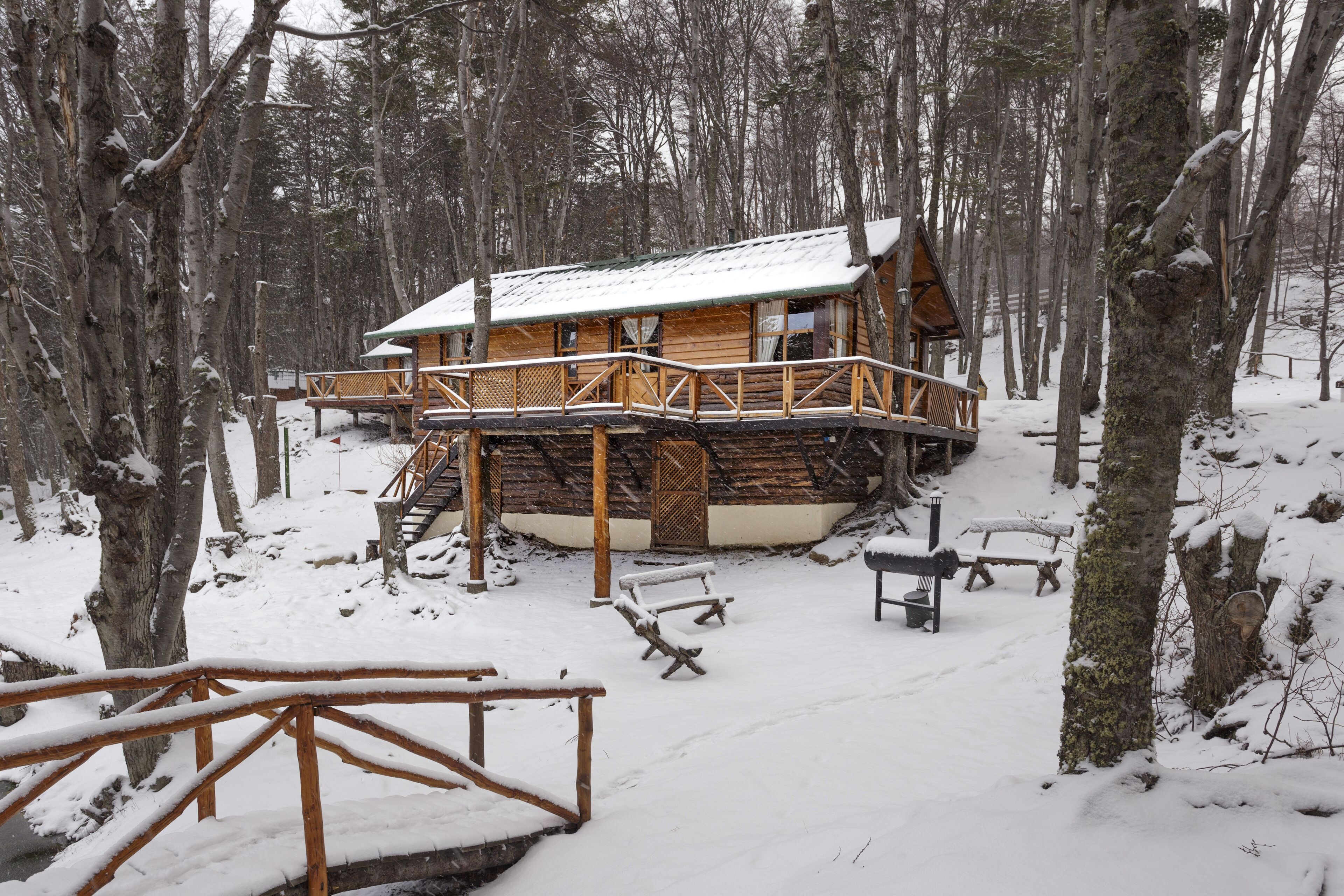 A wooden cabin with a deck, surrounded by snow-covered trees.