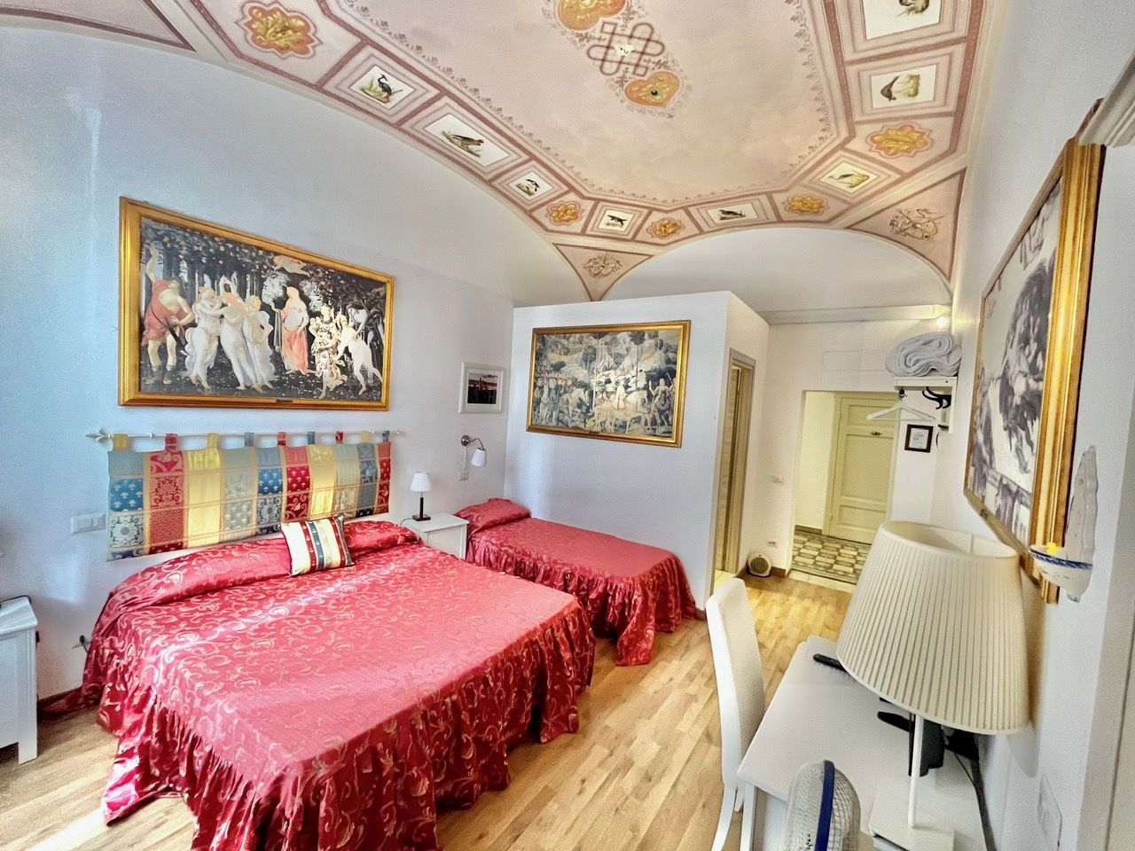 A hotel room with two beds, a desk, a chair, and a ceiling with decorative patterns.