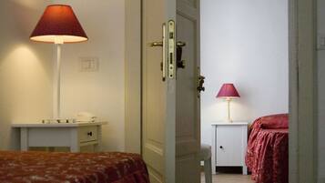 Ein Hotelzimmer mit einem Bett, einem Schreibtisch mit Lampe und einer Tür zu einem weiteren Raum.