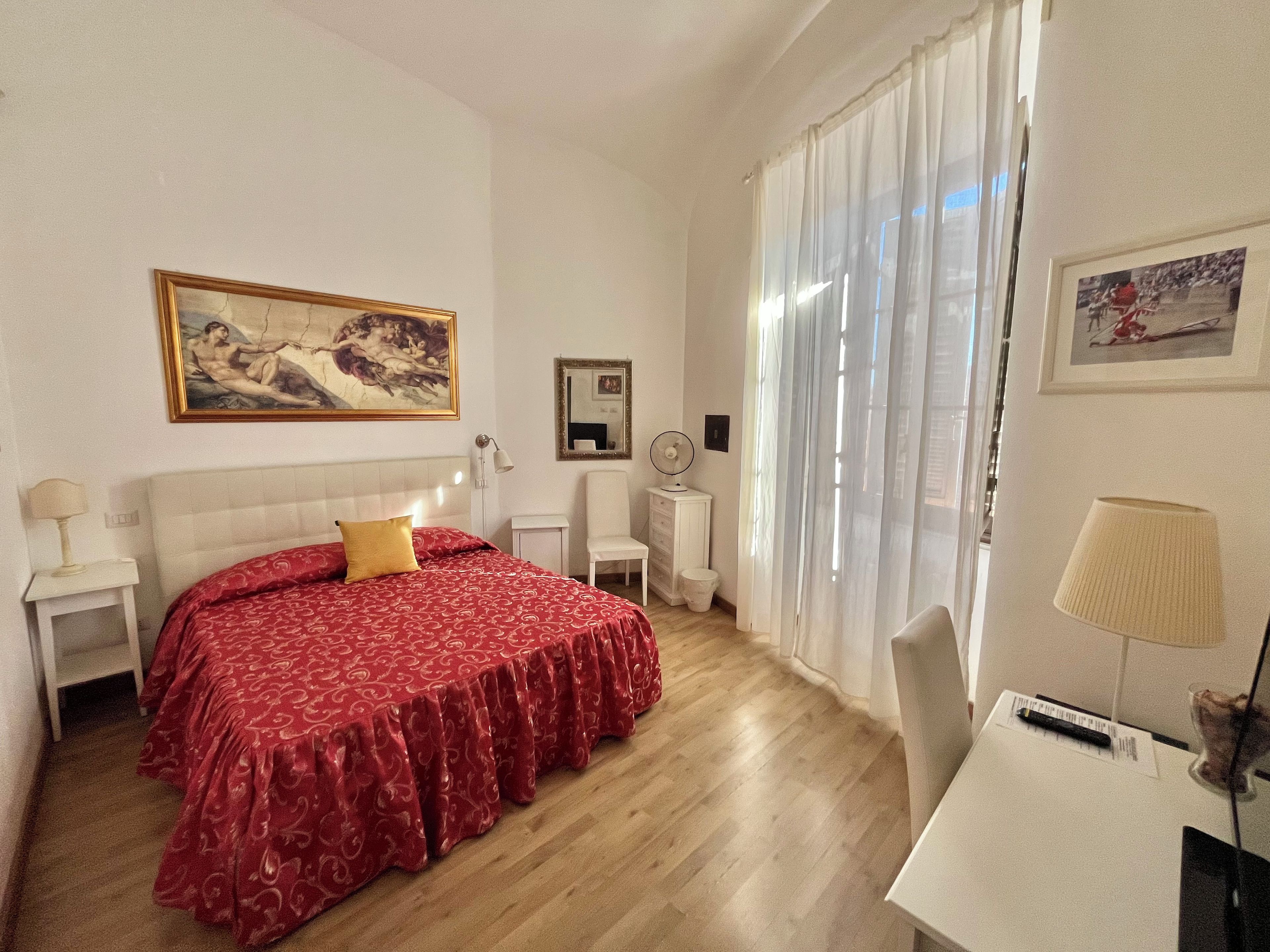 Habitación de hotel con una cama grande, un escritorio, una silla, una mesita de noche, una lámpara, un espejo y una ventana con cortinas.