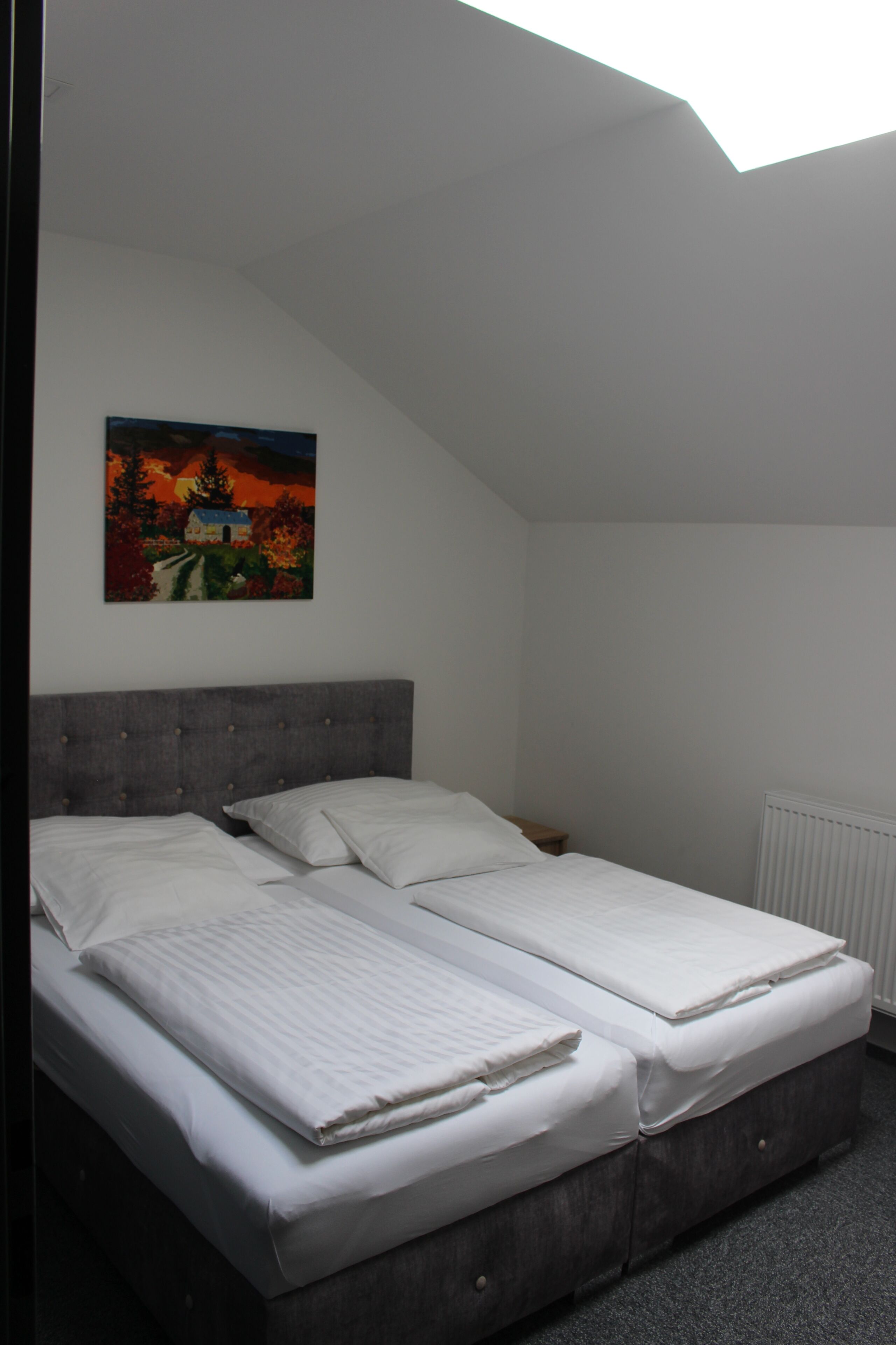 Una camera da letto con due letti, una testiera grigia e un quadro appeso al muro.