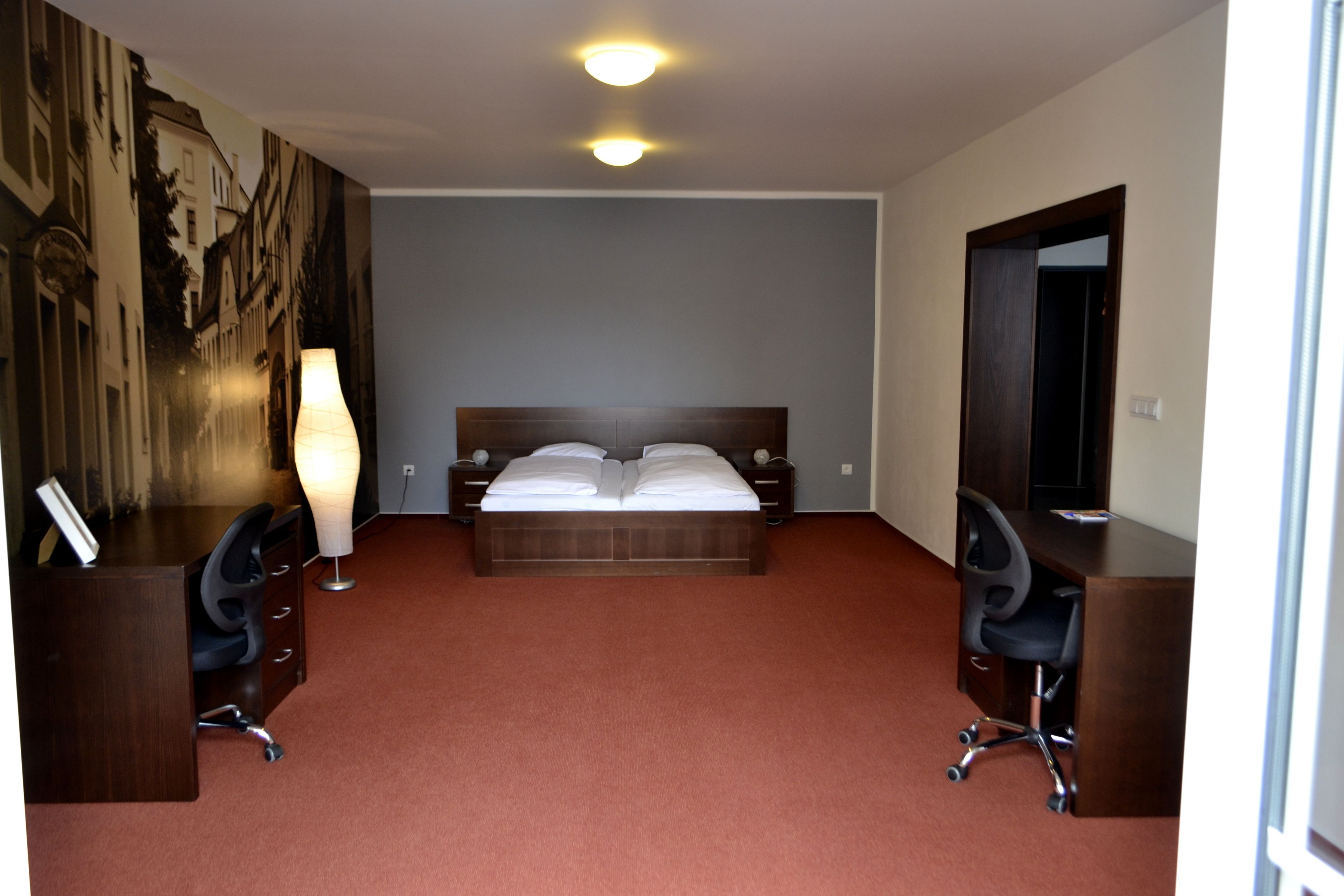 A hotel room with a large bed, two bedside tables, a desk with a chair, a standing lamp, and a large wall mural.