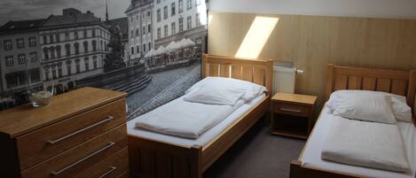 A room with two beds, a wooden dresser, a radiator, and a mural of a street scene.