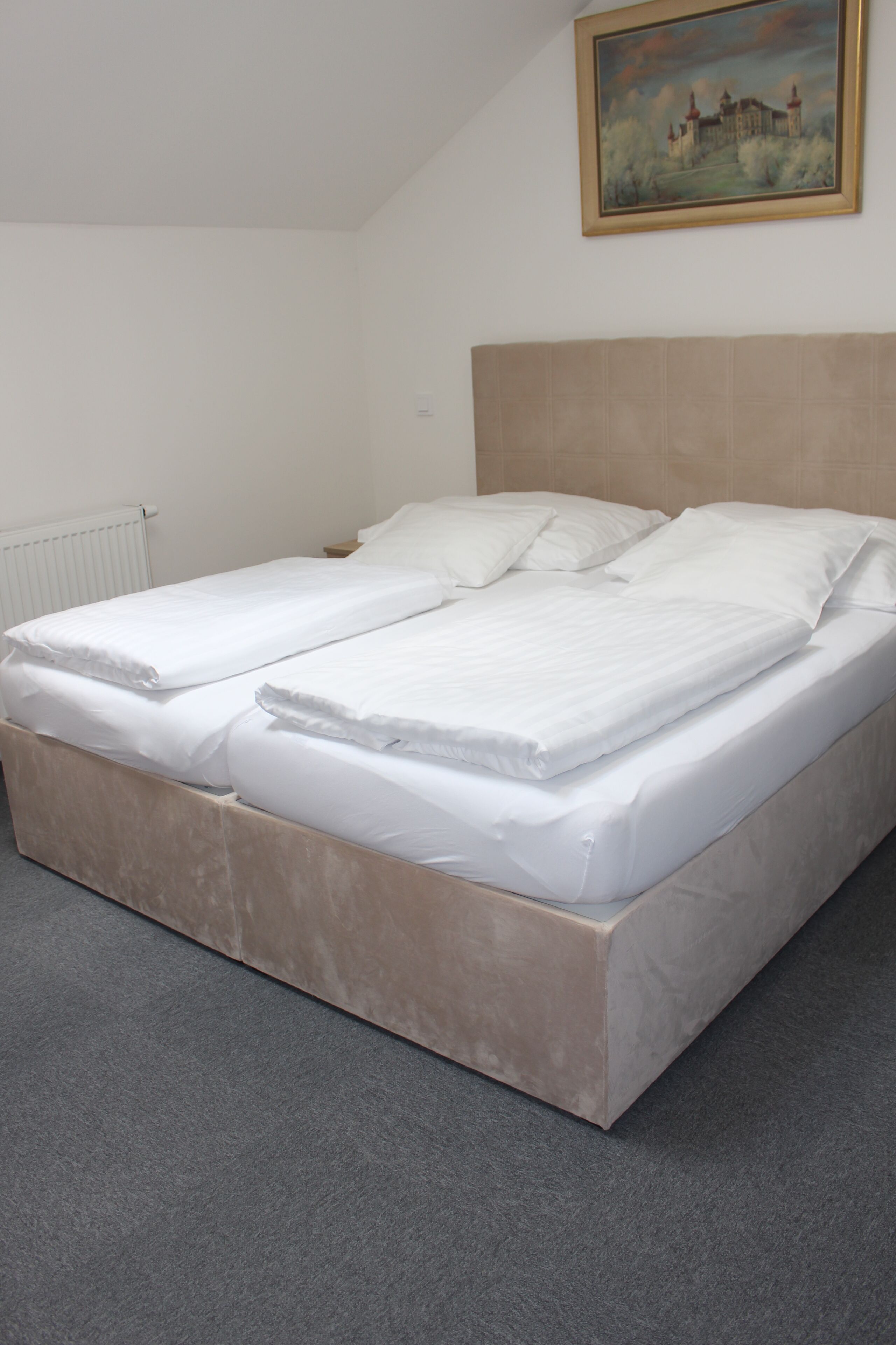 A single-bed room with a headboard, a radiator, and a painting on the wall.