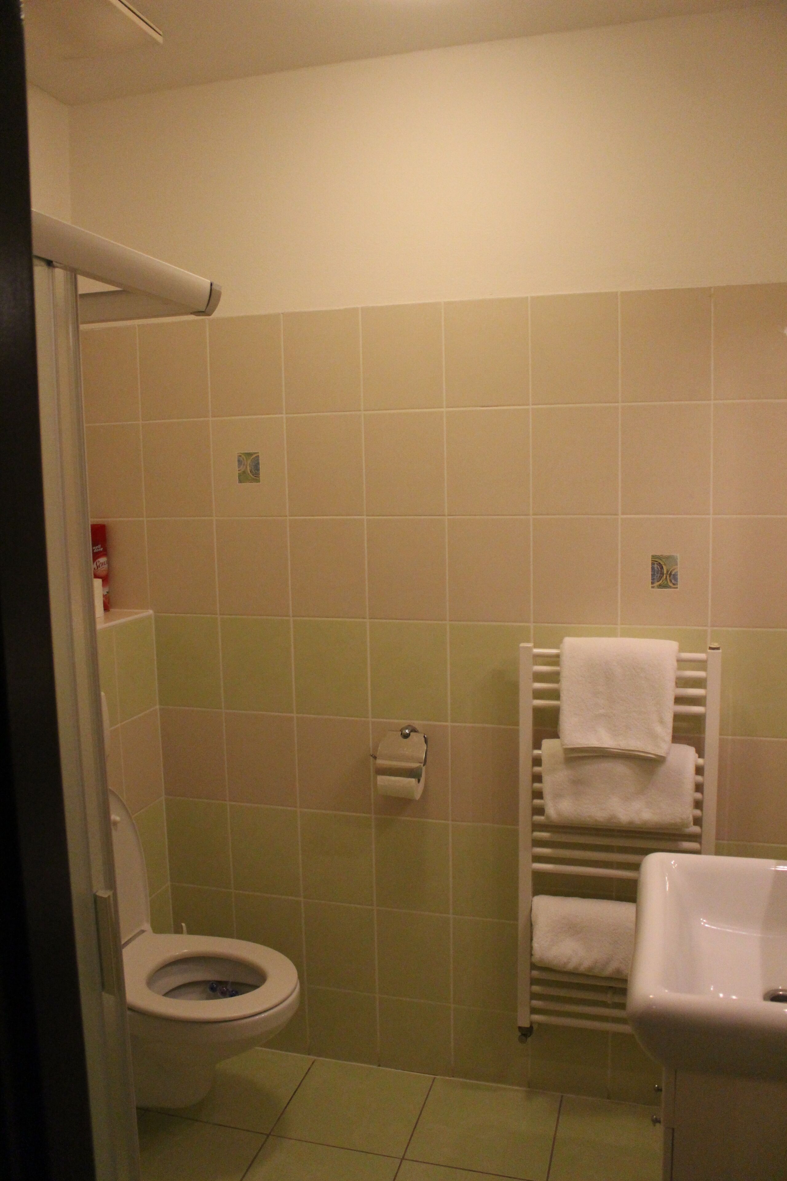 A bathroom with a toilet, a towel rack with towels, and a sink.