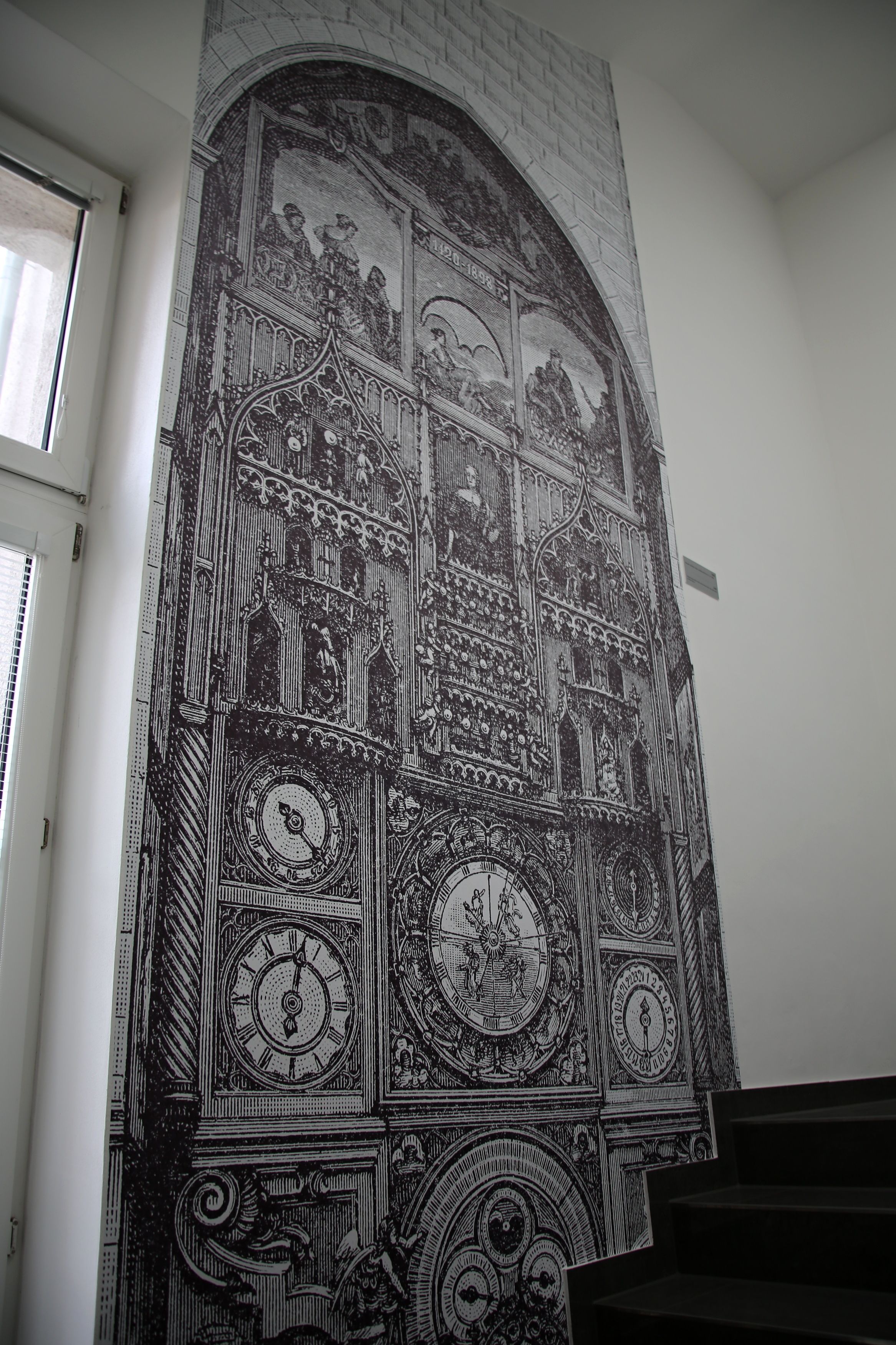 A detailed black and white mural with architectural and astronomical themes, including clocks and figures, on a wall.