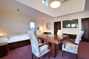 A hotel room with a bed, a dining table with four chairs, a TV mounted on the wall, and a window with a view.