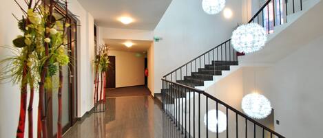 Un interior moderno con piso pulido, una escalera con barandillas negras y luces decorativas esféricas.