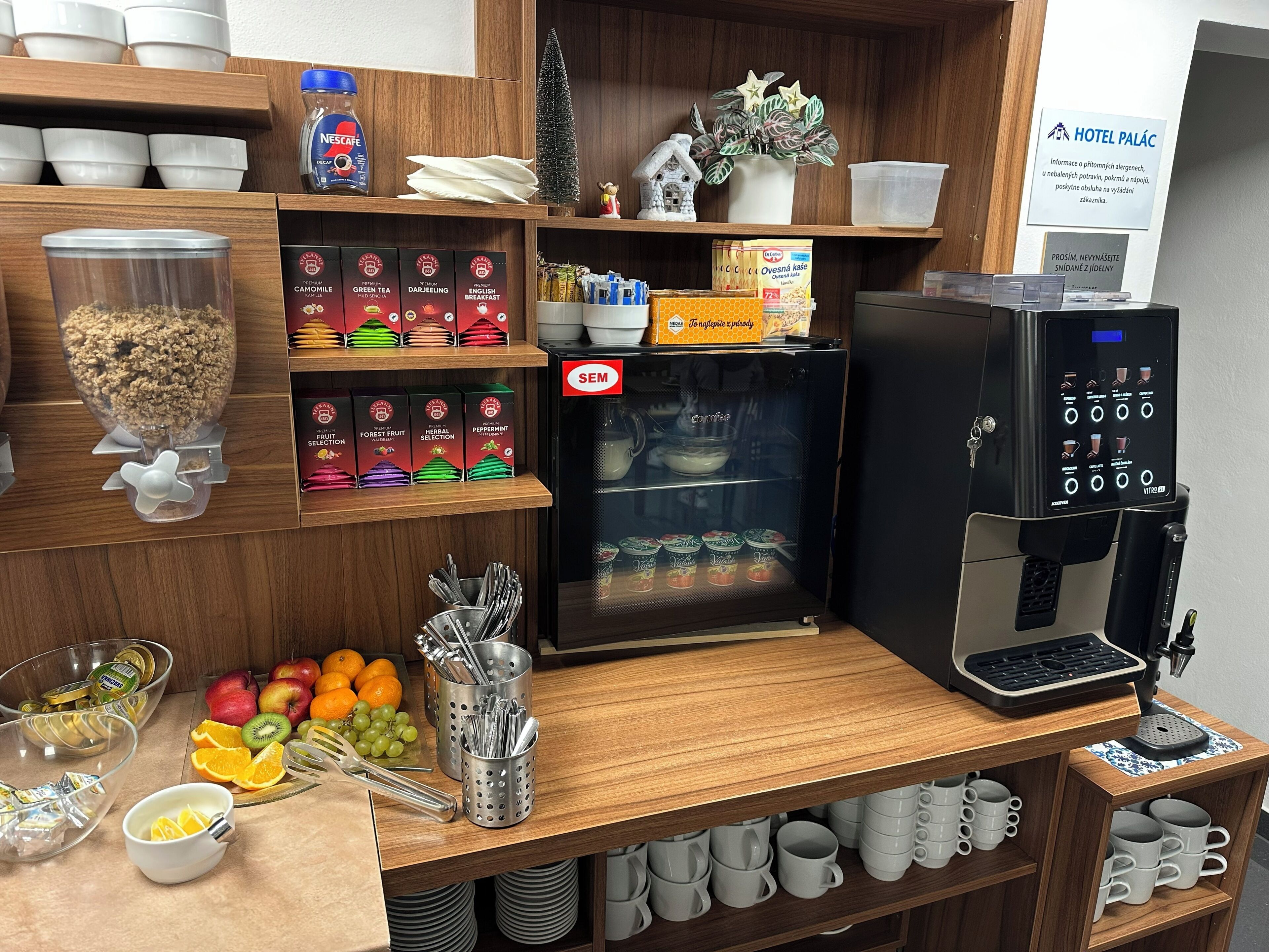 A breakfast bar with a coffee machine, various food items, and a sign indicating the hotel name.