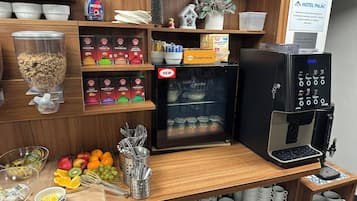 A breakfast bar with a coffee machine, various food items, and a sign indicating the hotel name.