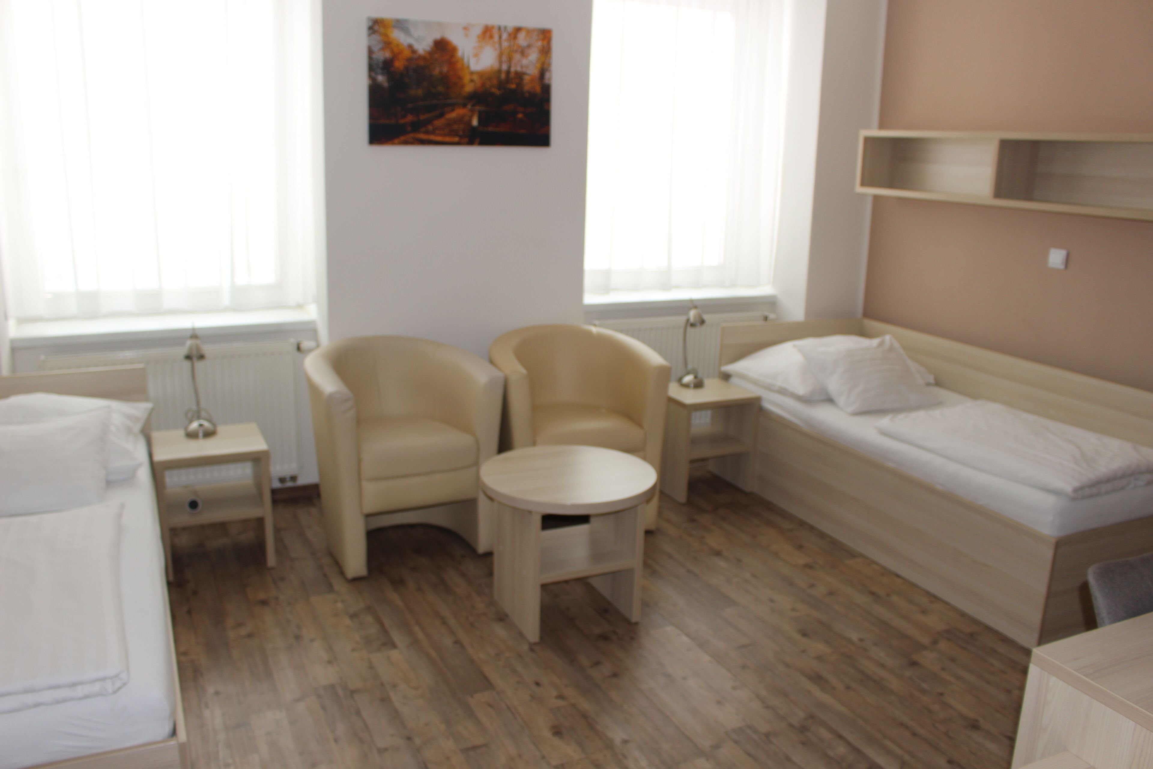 A room with a bed, two armchairs, a small table, and a painting on the wall.
