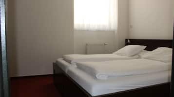 A single bed with white bedding in a room with a radiator and a window with sheer curtains.