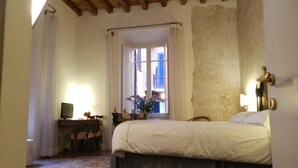 A bedroom with a bed, a desk with a computer, a window with curtains, and a view of the outside. - Vicolo del lupo Guesthouse (Rome)