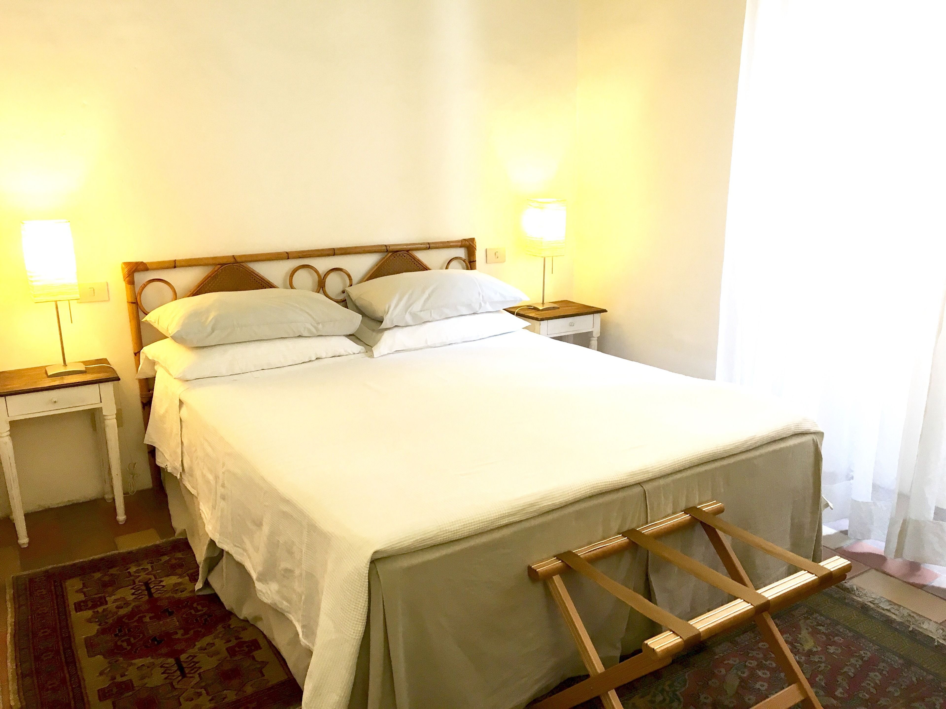 Un lit bien fait, avec du linge de lit blanc, deux tables de chevet avec des lampes et une tête de lit en bois.