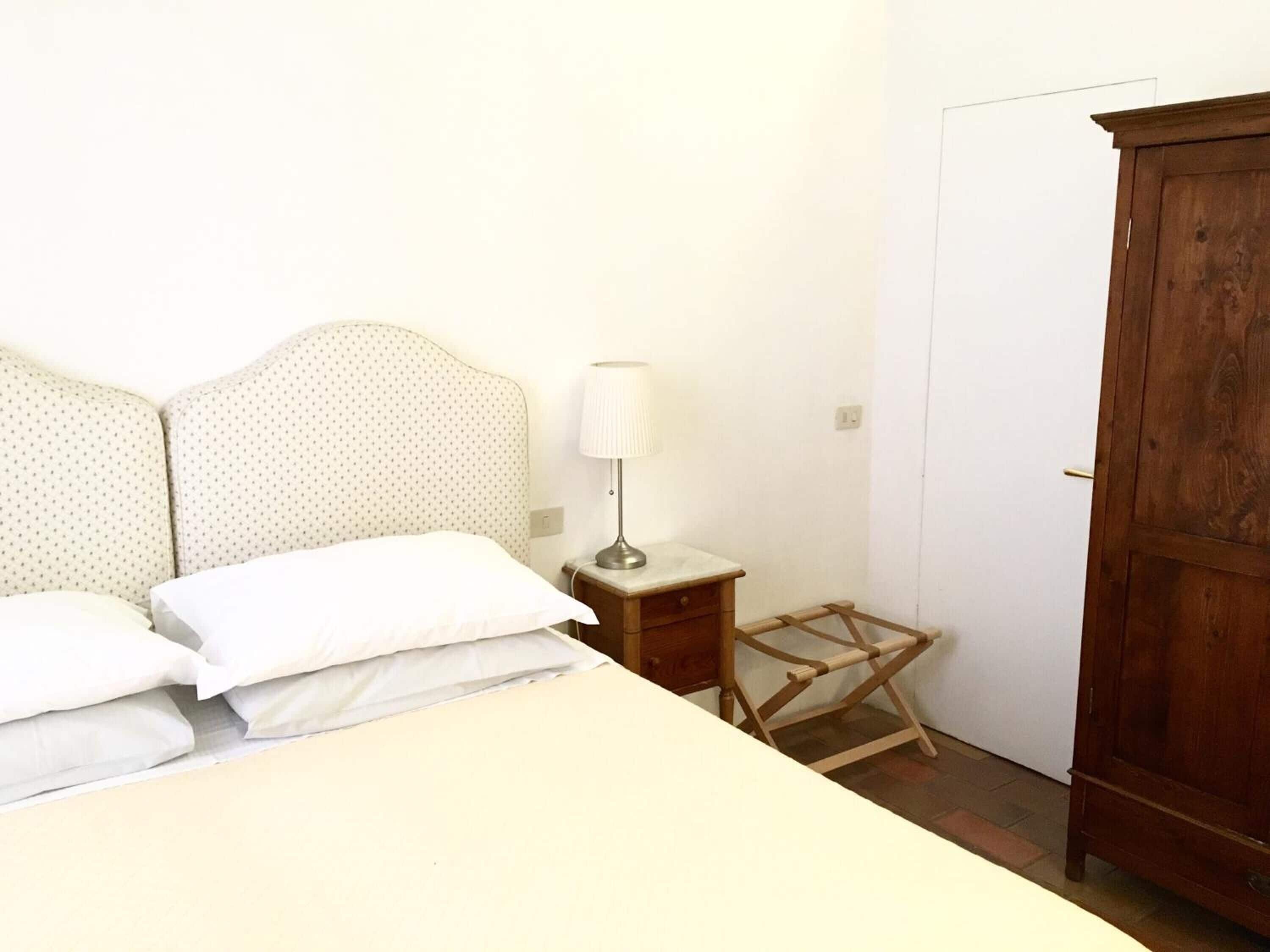 A bedroom with a bed, a nightstand, a lamp, and a wardrobe.
