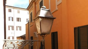 A narrow street with a building featuring a metal street lamp and shutters. - Vicolo del lupo Guesthouse (Rome)