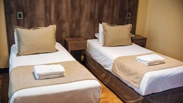 Habitación de hotel con dos camas, cada una con una almohada y una toalla doblada.