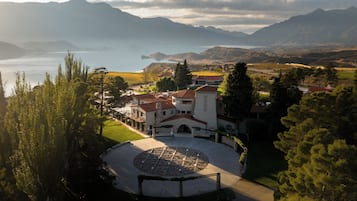 Un patio con un diseño circular de piedra, rodeado de edificios con tejados de tejas rojas, con montañas y un lago al fondo.