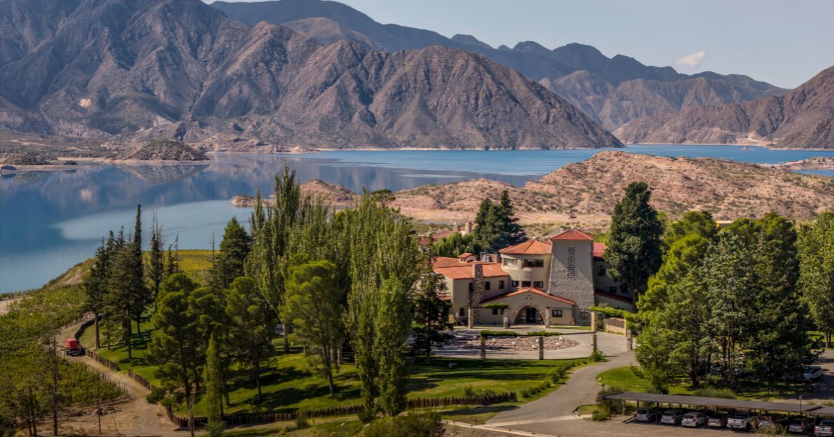 Un edificio con tejado rojo, rodeado de árboles y montañas al fondo.