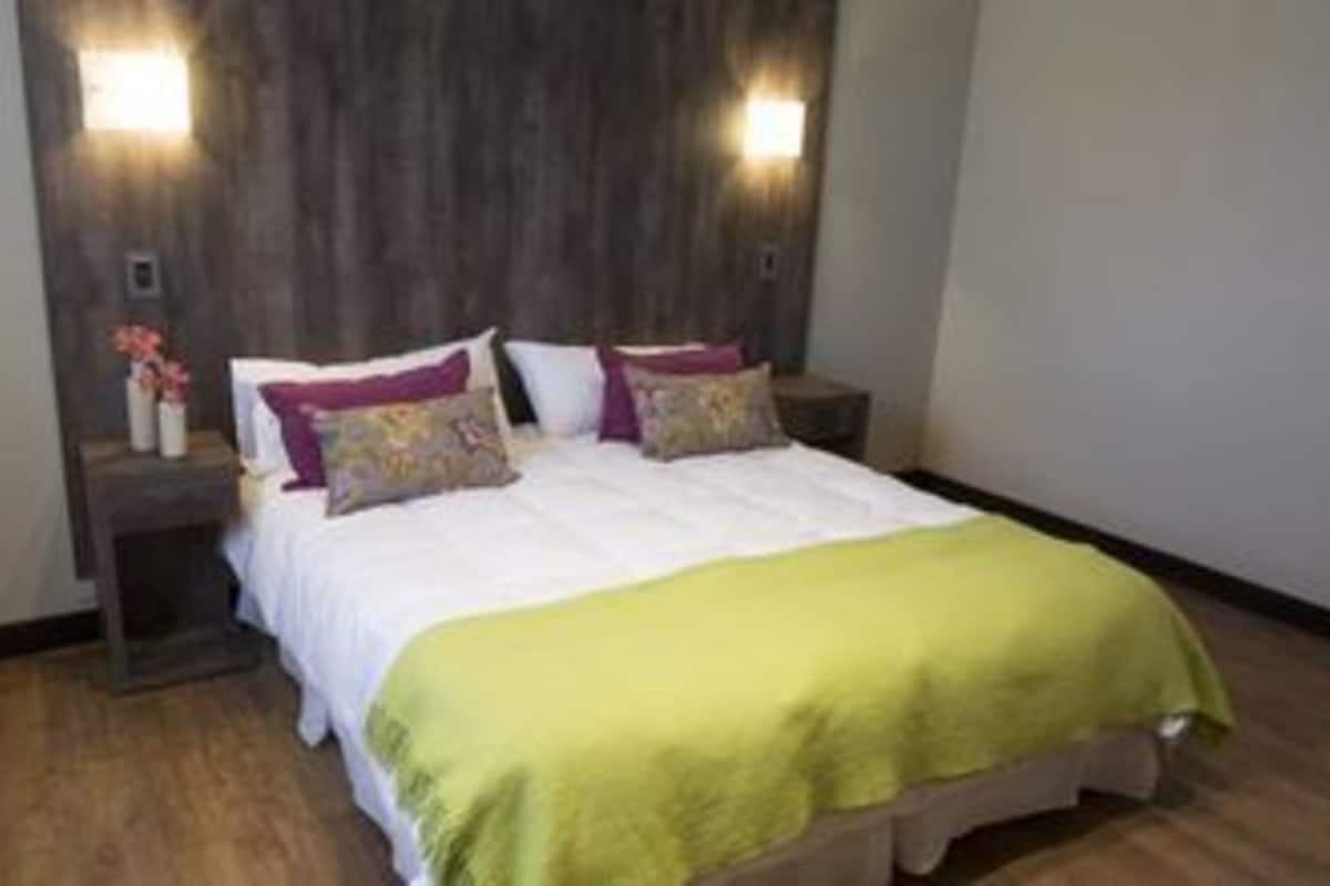 Una cama bien hecha con un plaid verde, dos lámparas de noche y un cabecero de madera.