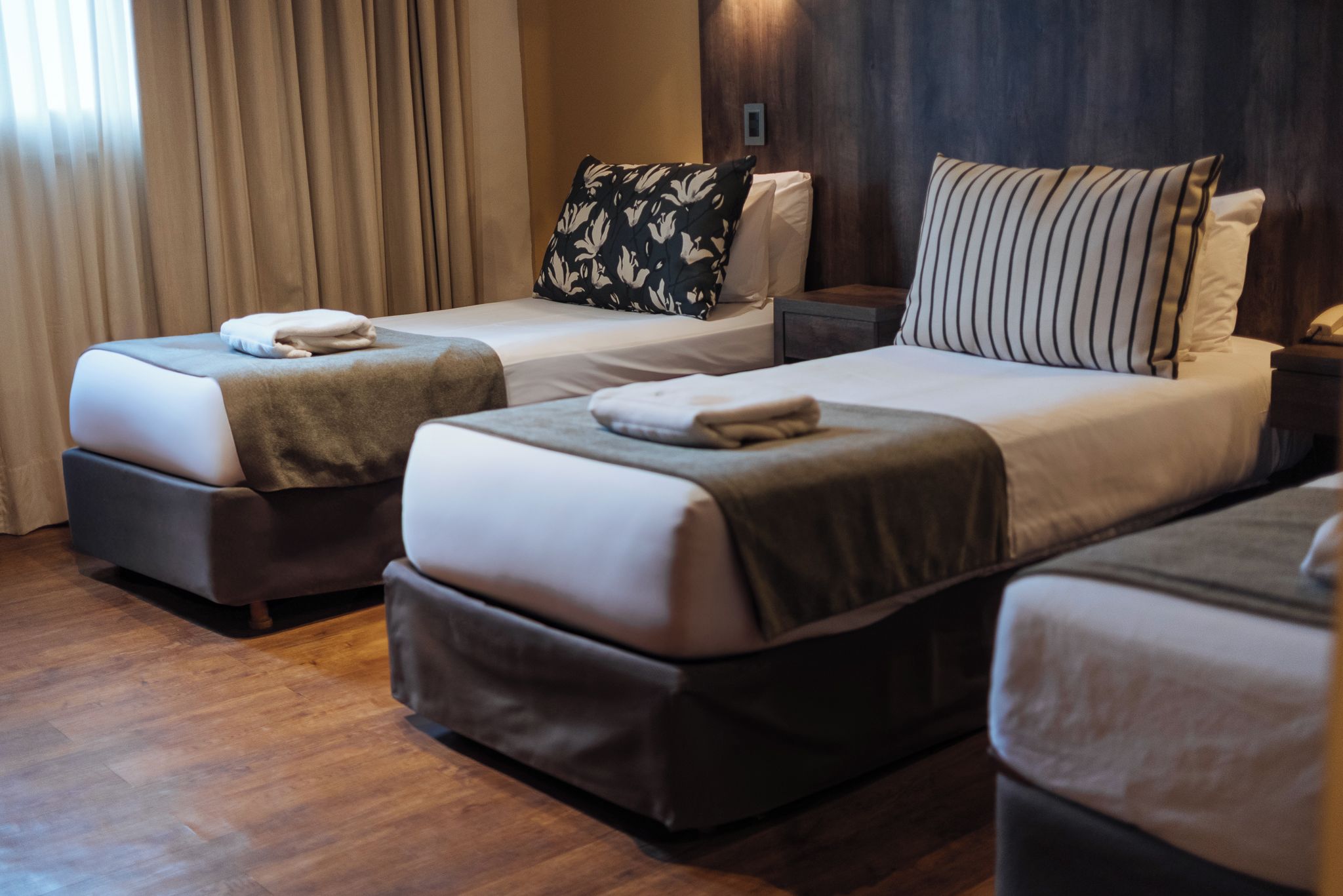 A hotel room with two beds, each with a pillow and a blanket.