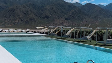 Una piscina con agua azul cristalina, rodeada de sillones de descanso y montañas al fondo.