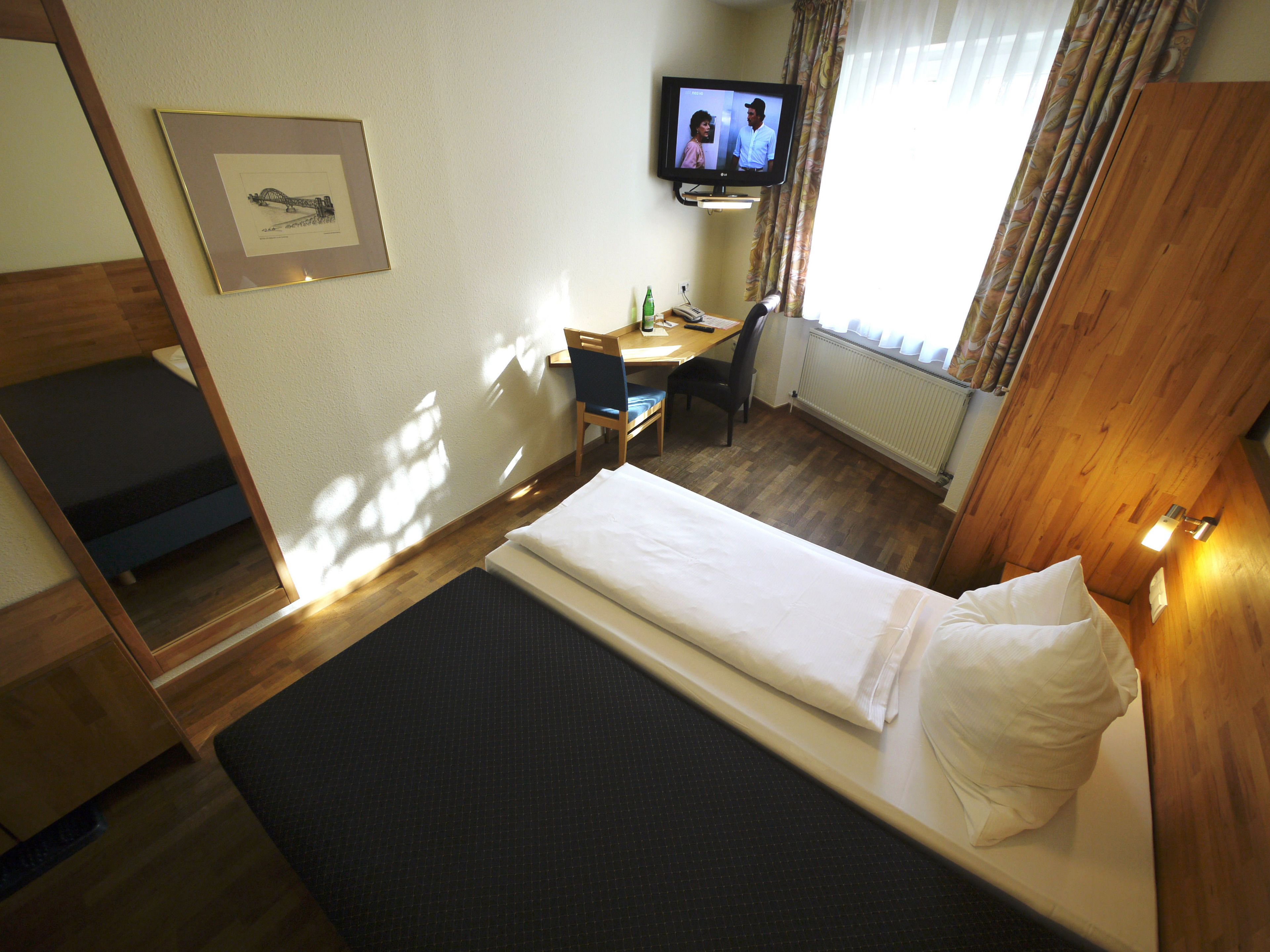 Ein Hotelzimmer mit Bett, Schreibtisch, Stuhl, Fernseher und einem gerahmten Bild an der Wand.