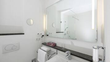 A modern bathroom with a large mirror, a towel rack, a sink, and a glass of water on the counter.