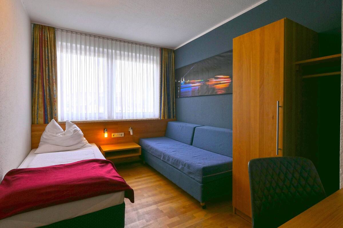 Une chambre d’hôtel de taille réduite, comprenant un lit, un canapé, une petite table et une armoire en bois.