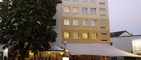 Un hotel chiamato 'hotel pinger' con diversi piani e un grande albero di fronte.