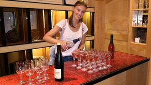 A person pouring wine into glasses on a red table in a room with wooden shelves and framed certificates. - Hotel Pinger (Remagen)