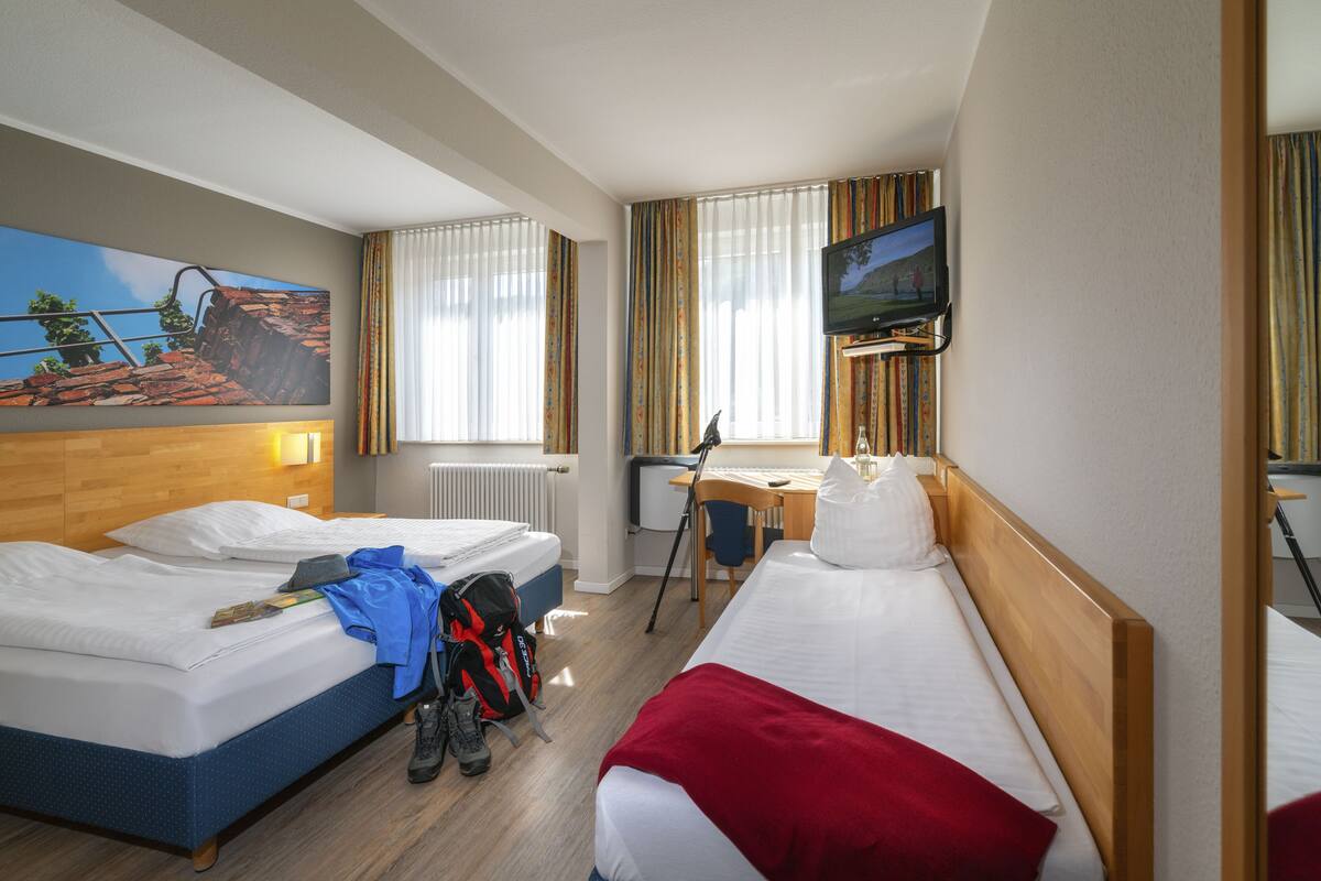 Une chambre d’hôtel avec deux lits, un bureau, une télévision et un tableau au mur.