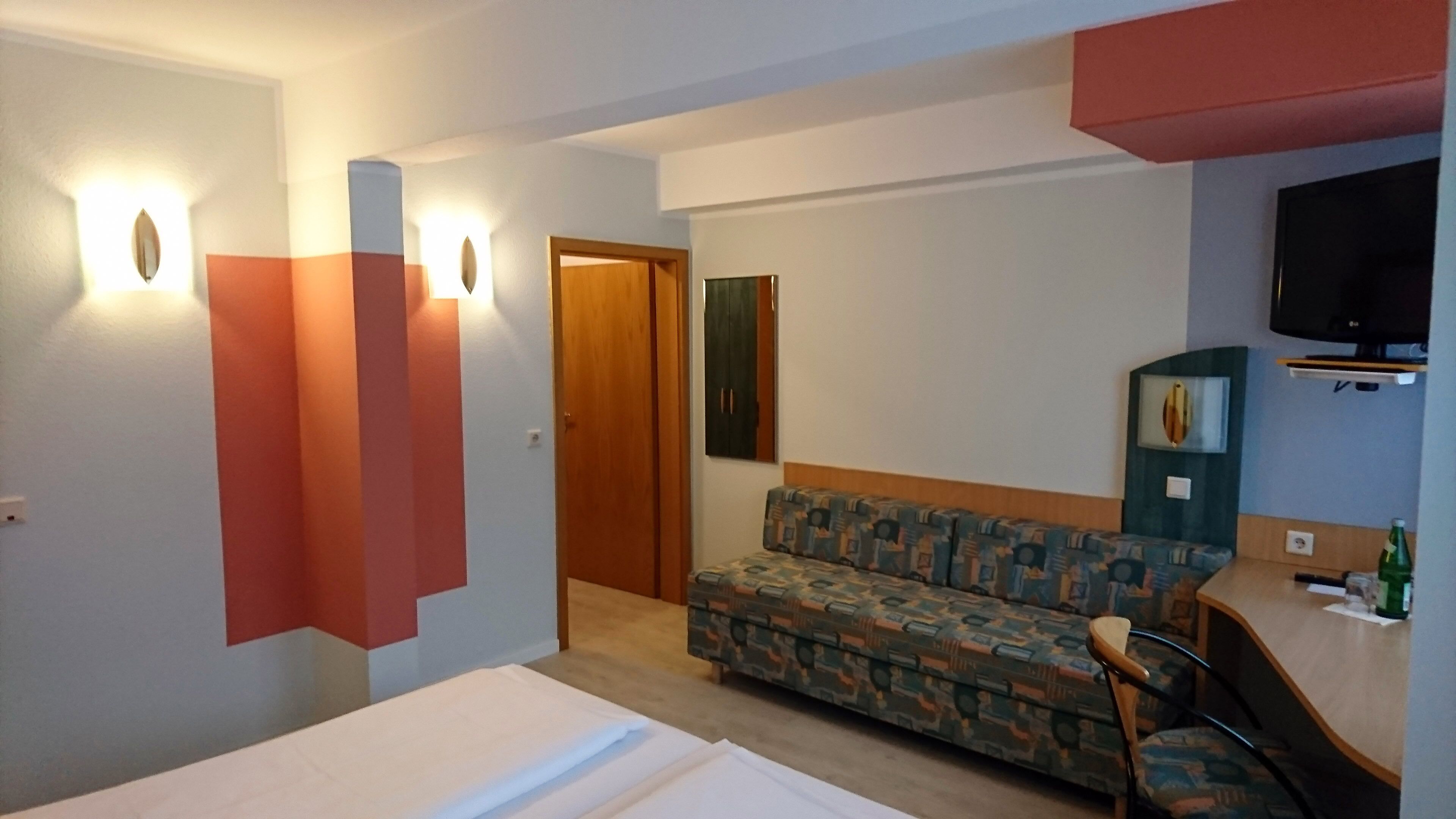 Una habitación de hotel con un sofá, una televisión, un escritorio y una puerta.