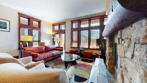 A cozy living room with a red leather sofa, a glass coffee table, and a stone fireplace.
