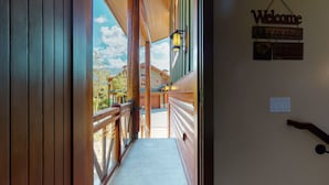 A wooden exterior corridor with a 'Welcome' sign, a lantern, and a view of a building with a green roof.