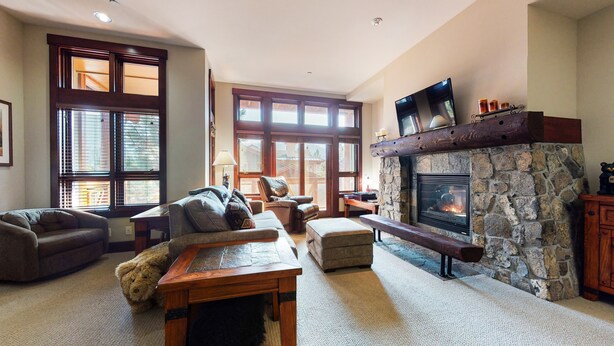 A spacious living room with a stone fireplace, large windows, and comfortable seating. - Juniper Crest 6 3 Bedroom Townhouse by RedAwning (Mammoth Lakes)